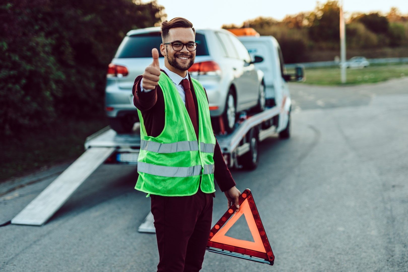 A man is giving a thumbs up in front of a tow truck.
