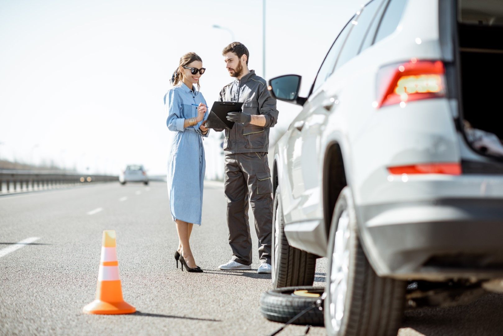 A man and a woman are standing next to a broken down car on the side of the road.